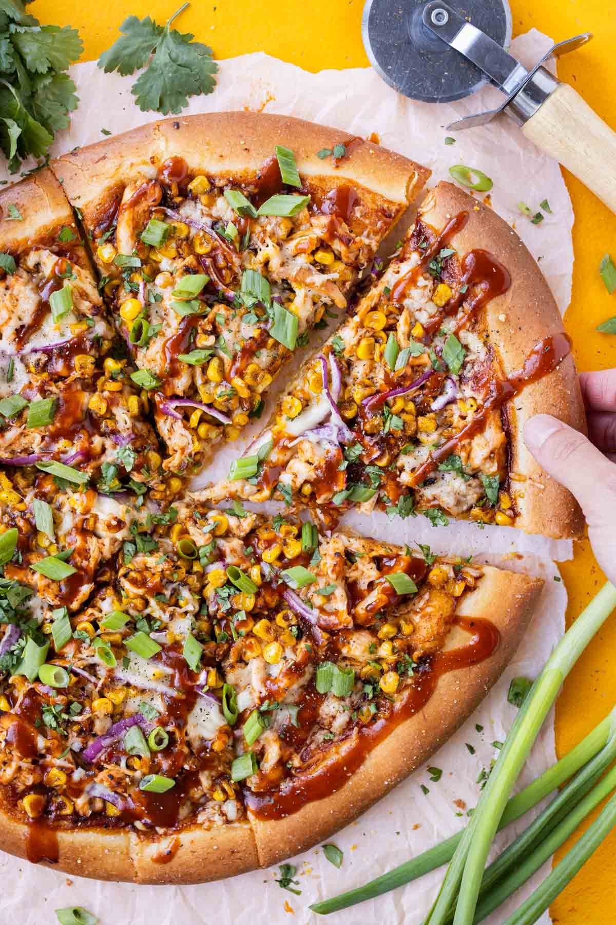 A homemade BBQ chicken pizza with roasted summer corn is being picked up.