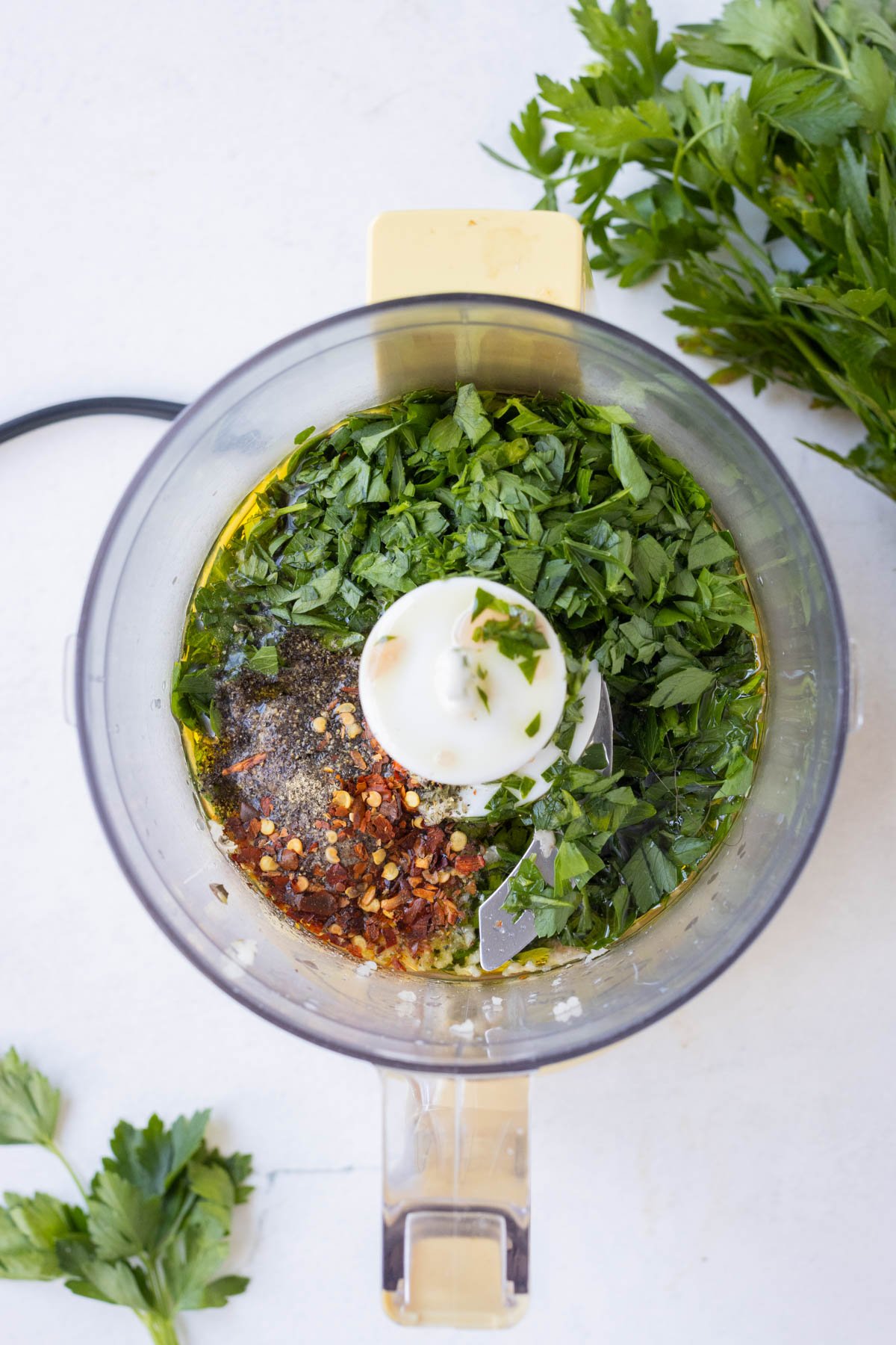 The chimichurri sauce ingredients are added to a food processor bowl.