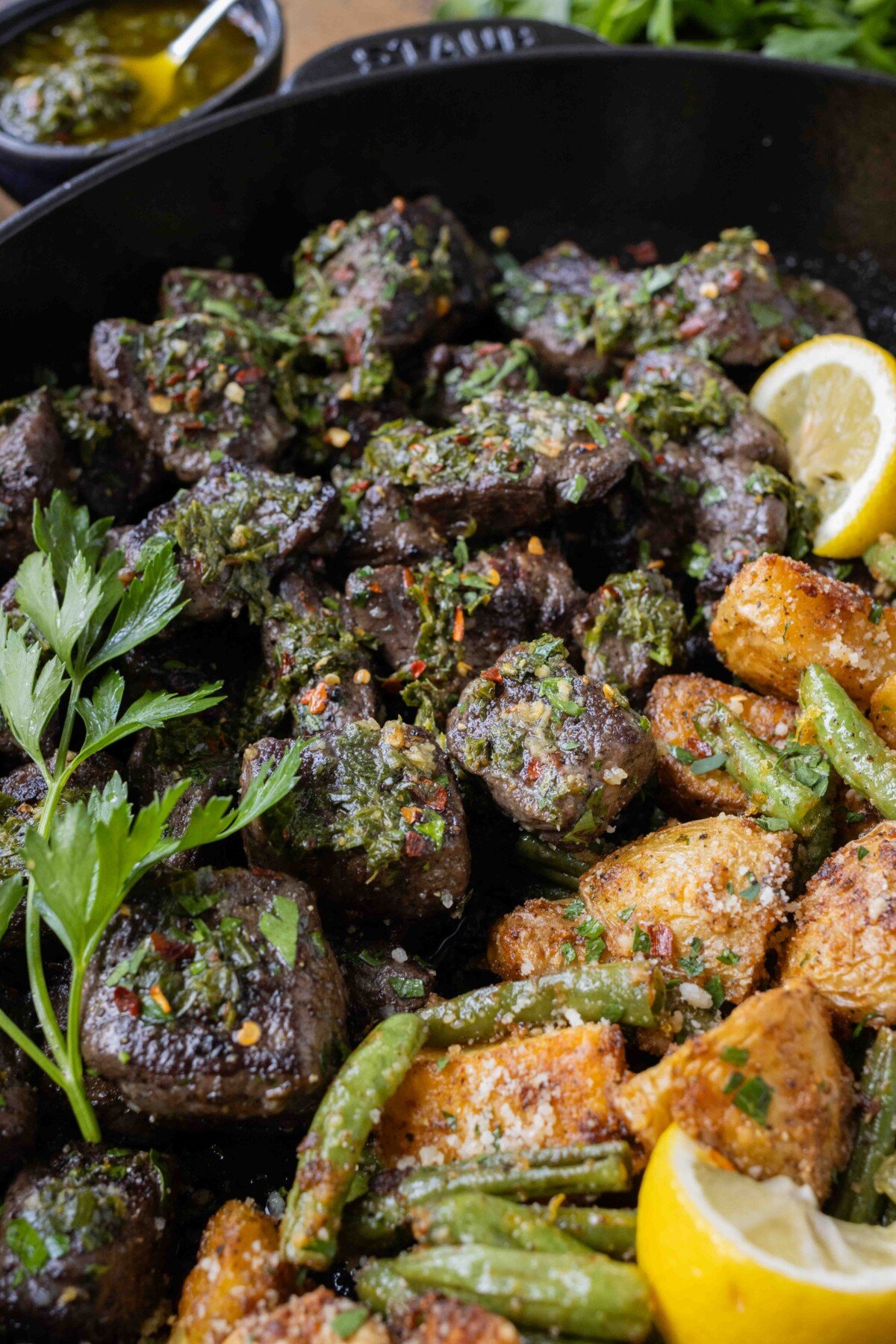 Steak bites in a skillet with chimichurri sauce drizzled on top.