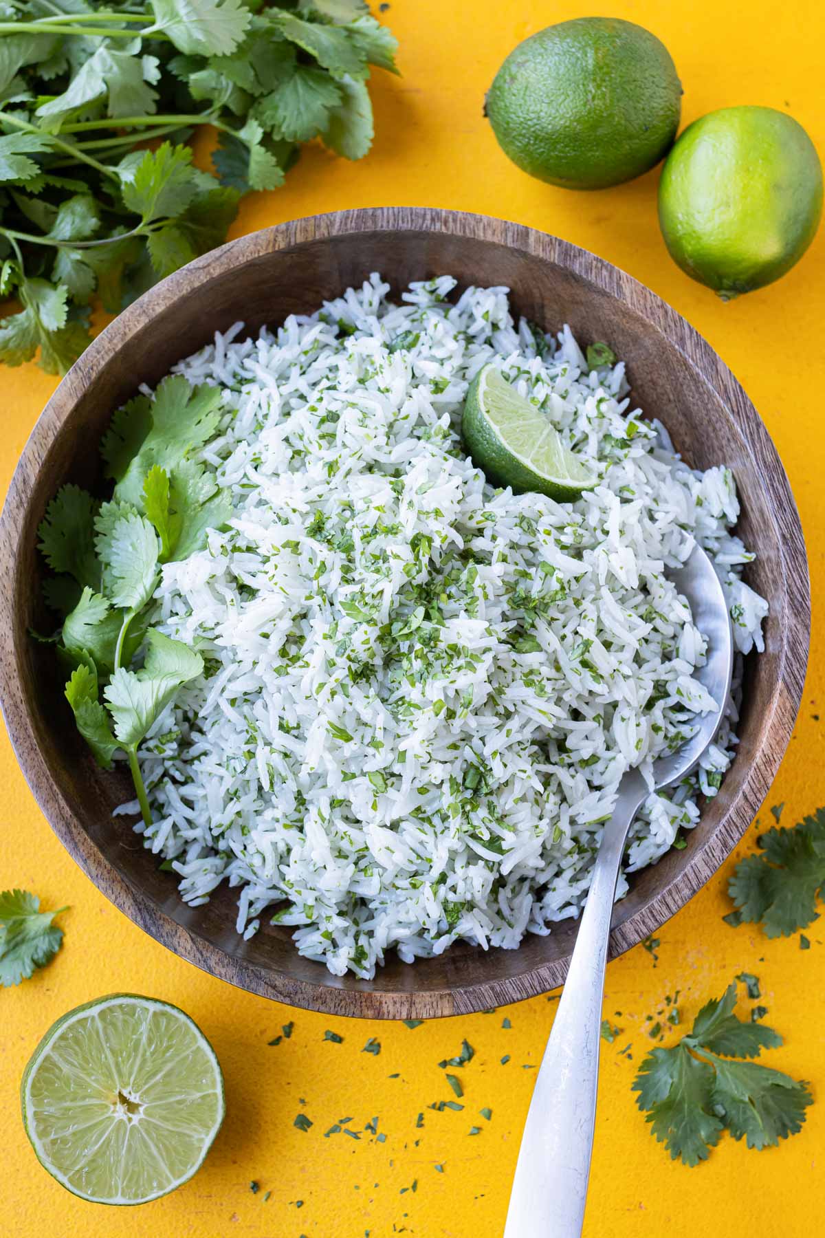 A wooden bowl full of coconut milk cilantro lime rice sits nexto to limes and a bunch of cilantro.