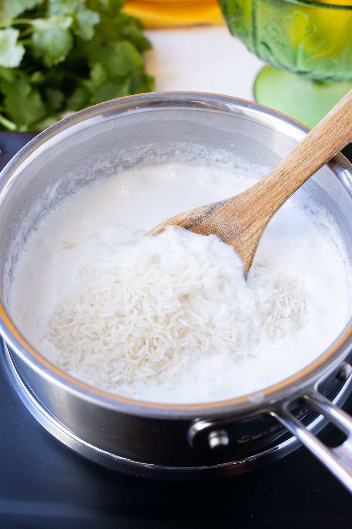 A wooden spoon stirs together the ingredients for coconut milk cilantro lime rice in a pot.