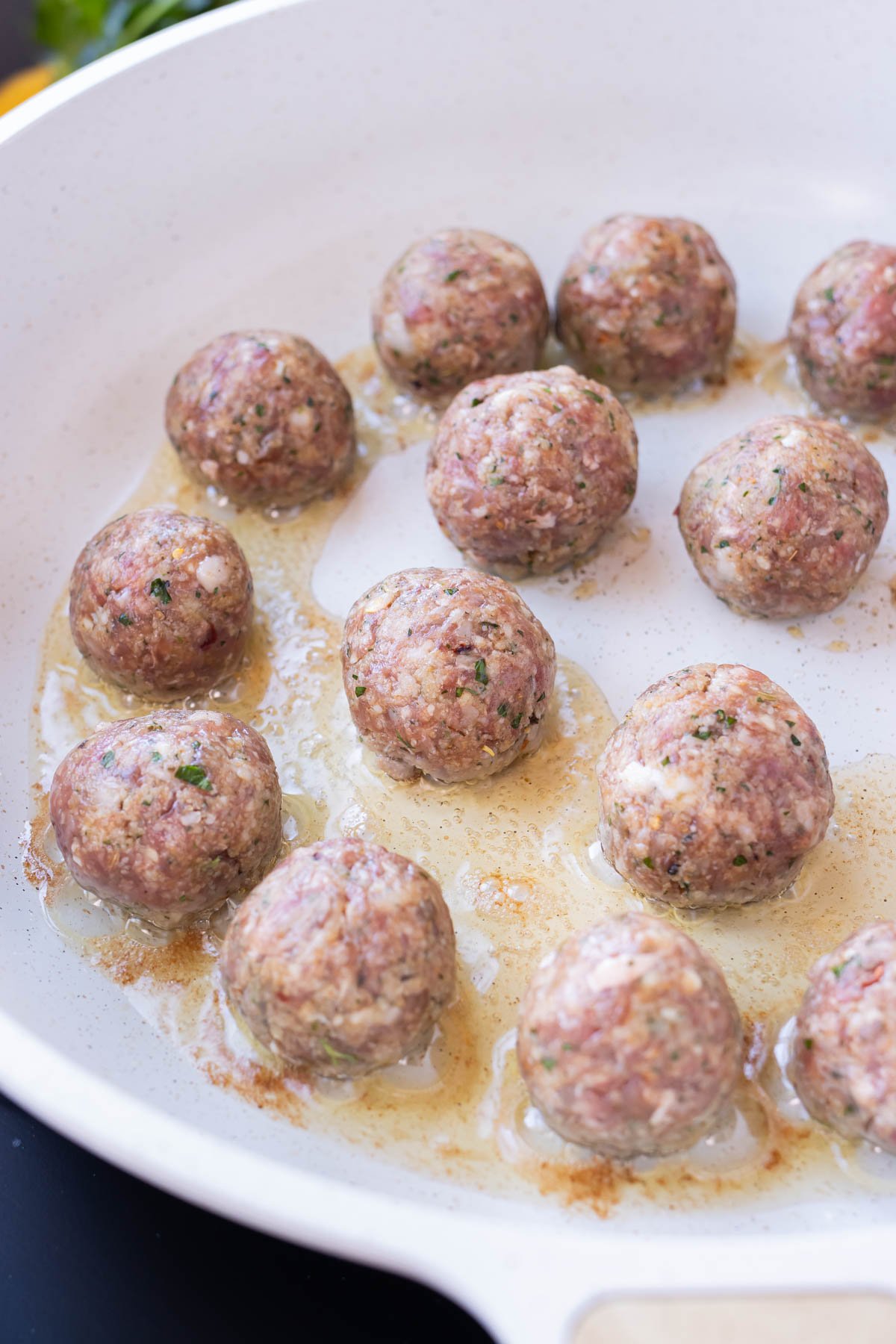Italian meatballs are seared in a skillet on the stovetop.