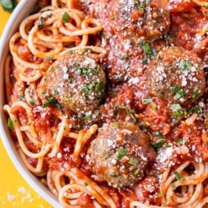 A bowl of spaghetti and marinara sauce with four Italian meatballs with Parmesan cheese.