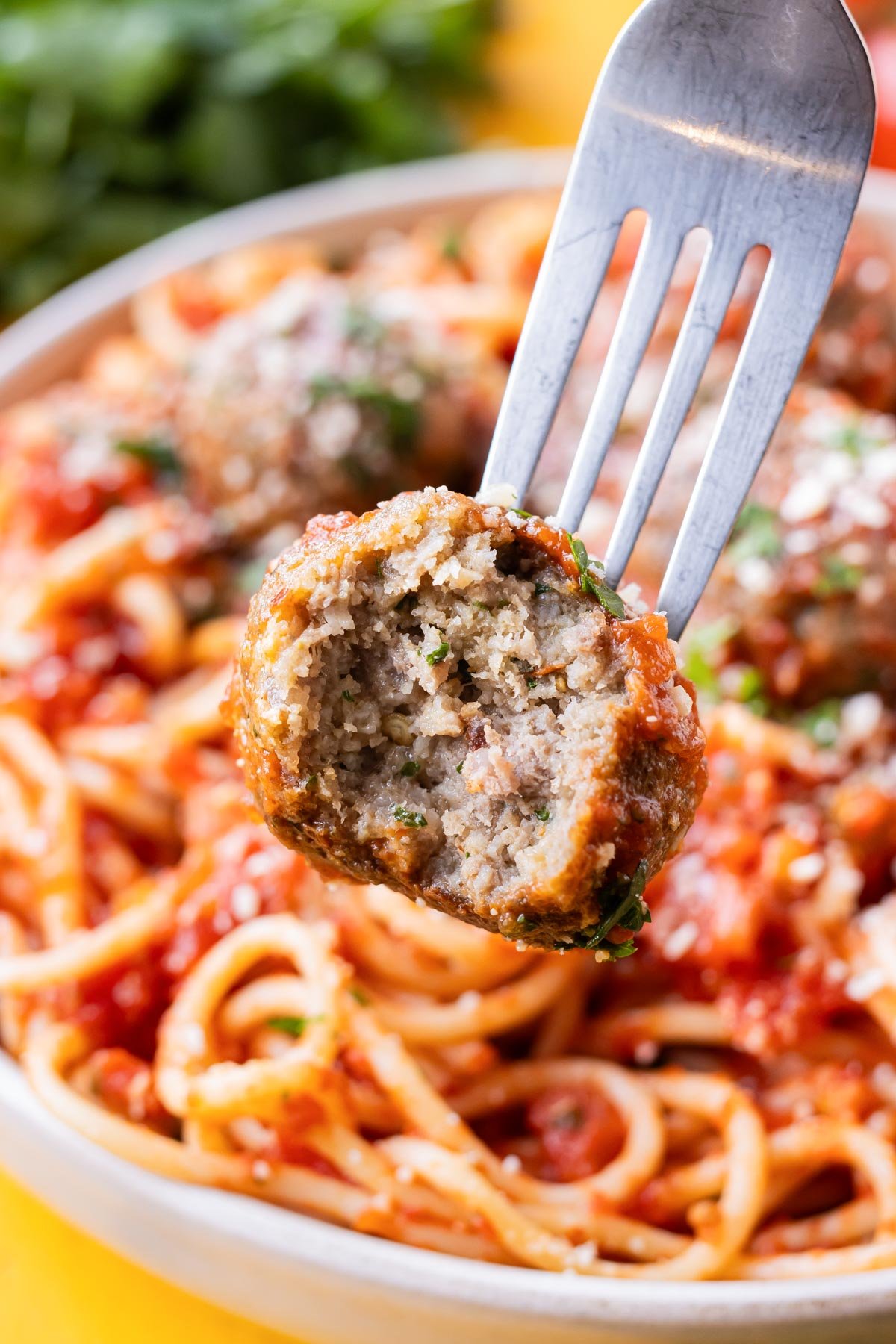 A fork picks up an Italian meatball made from an easy recipe with a bite taken out.