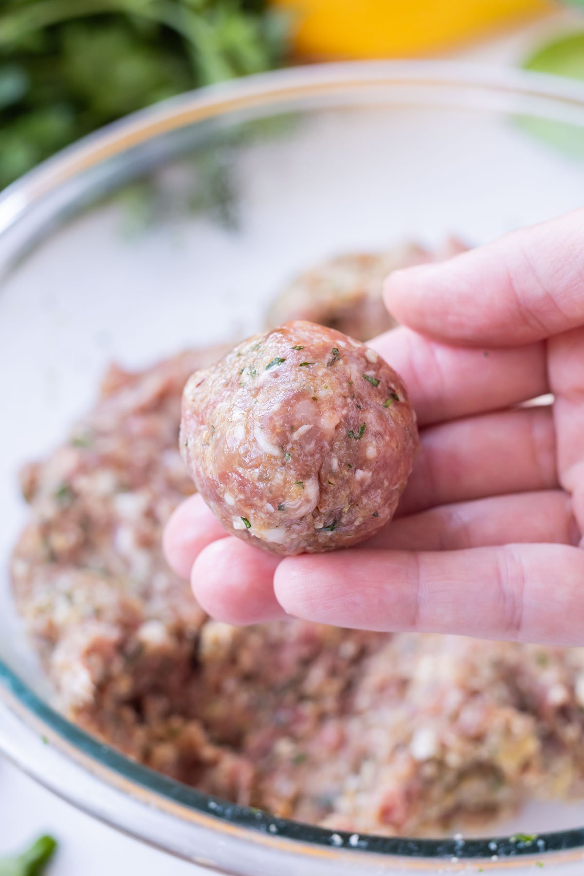 A hand is holding a meatball after it has been formed.
