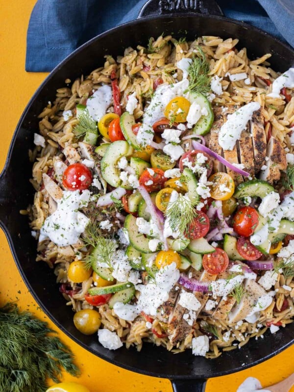 A Greek Shawarma Chicken Orzo Skillet with cucumber salad and a dill yogurt sauce is served for dinner.
