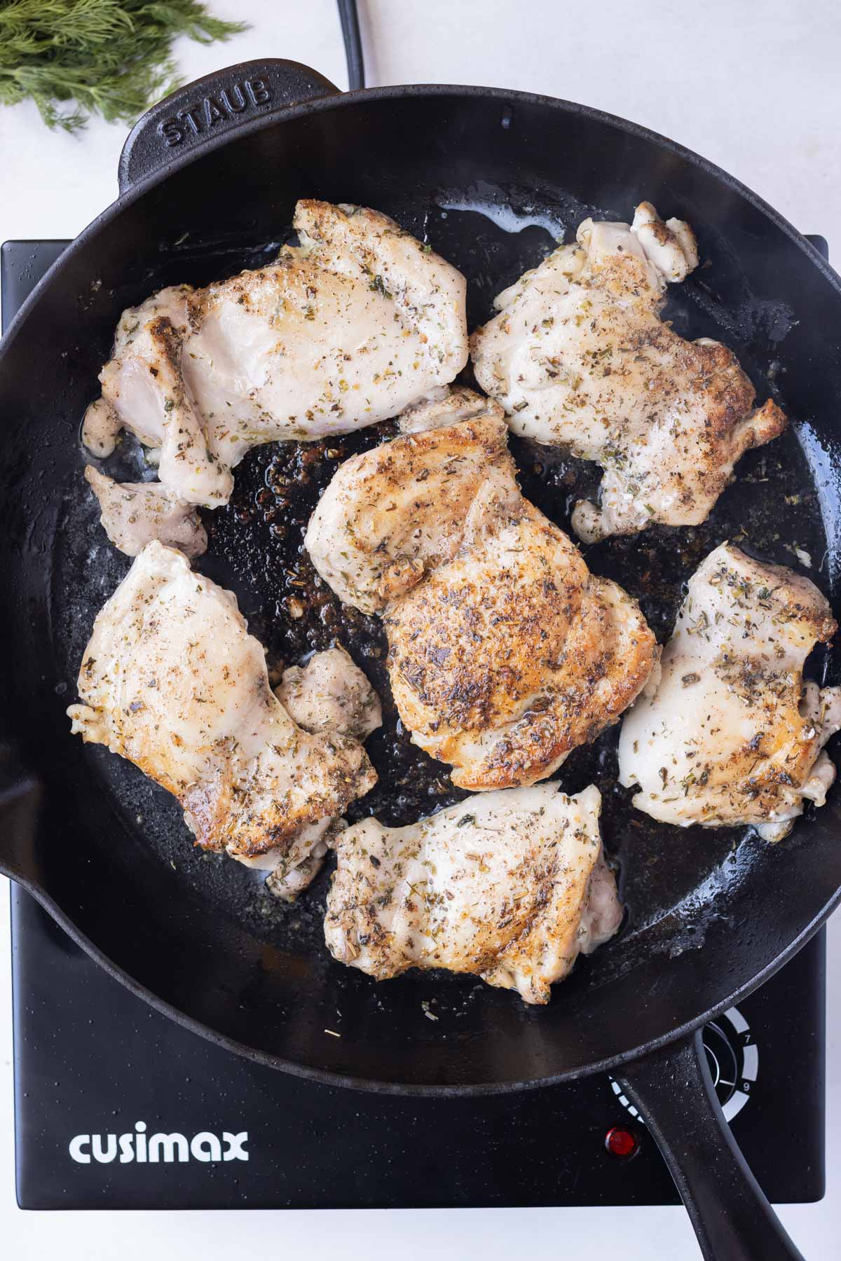 Seasoned chicken thighs are cooked in a skillet.