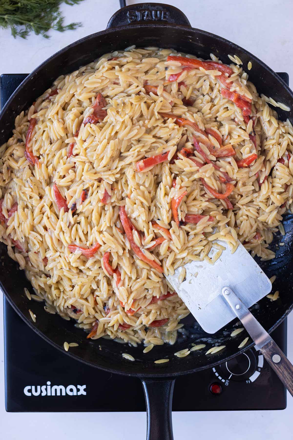 A spatula stirs together the orzo dish.