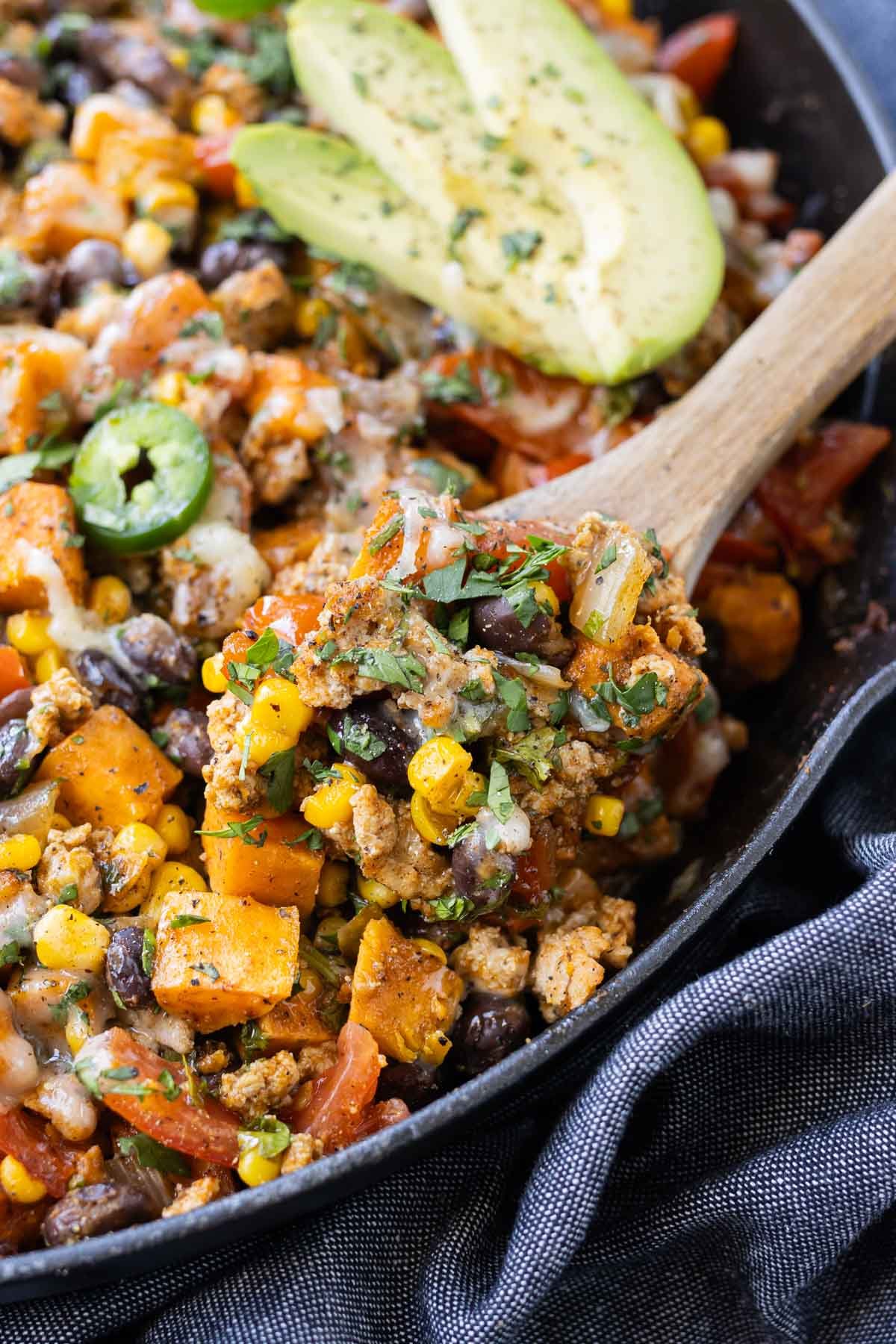 A spoon scoops up a Ground Turkey Sweet Potato skillet recipe with black beans, cheese, and corn.