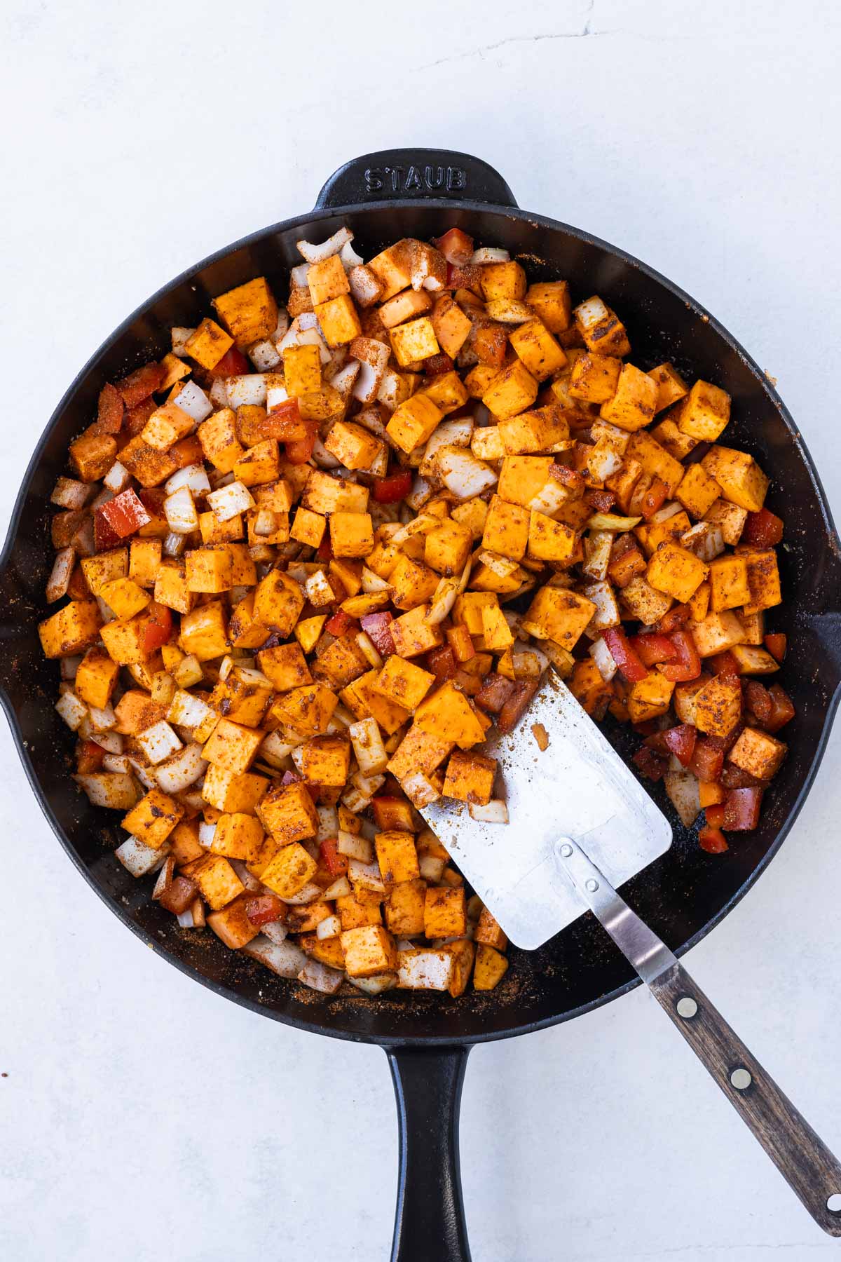 A spatula stirs the sweet potato and veggie mixture.