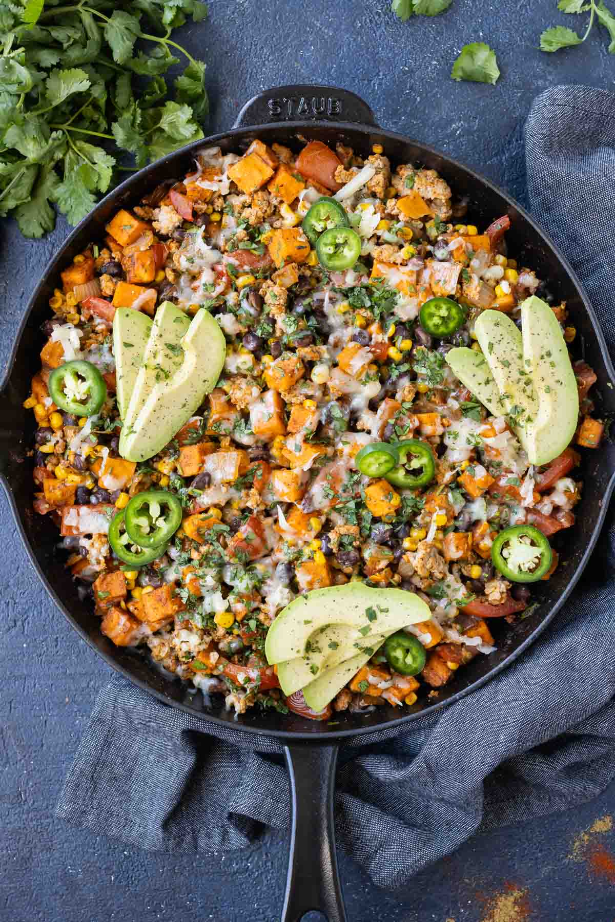 A ground turkey sweet potato skillet is cooked in cast iron then topped with cilantro and avocado.