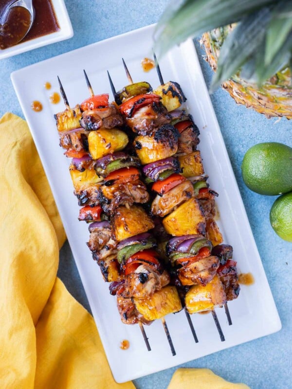 Hawaiian Chicken Kabobs are on a white plate with a soy marinade and pineapple next to them.