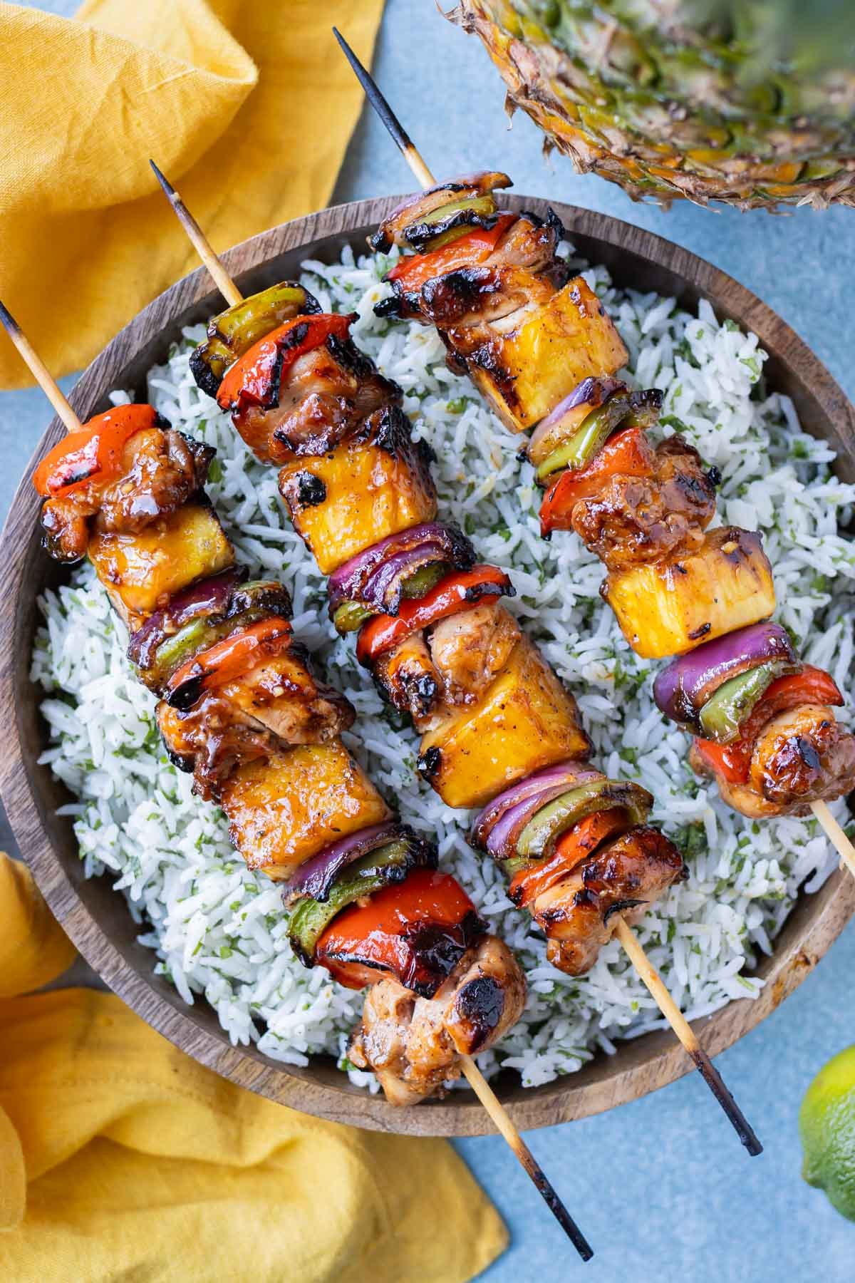 Hawaiian chicken kabobs are on a bed of rice next to a pineapple.