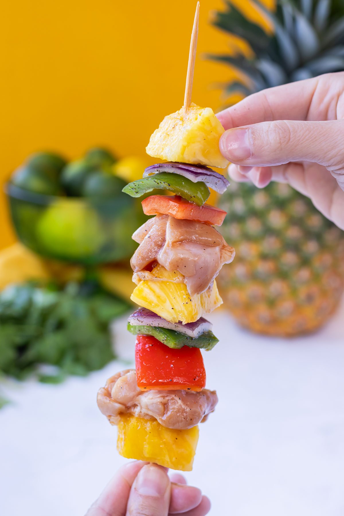 A hand holds a skewer full of chicken and veggies.