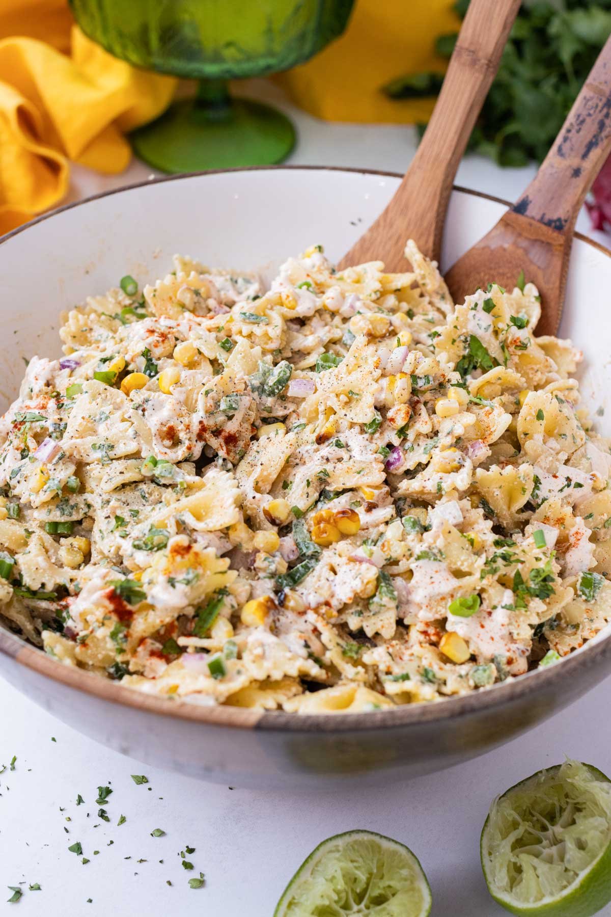 Wooden utensils stir up some Mexican street corn pasta salad in a white bowl.