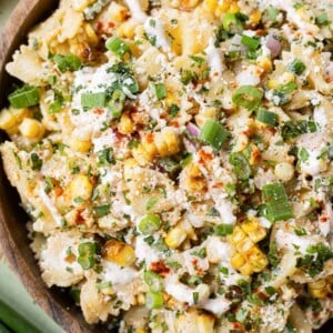A Mexican Street Corn Salad is being served in a wooden bowl with a spoon.
