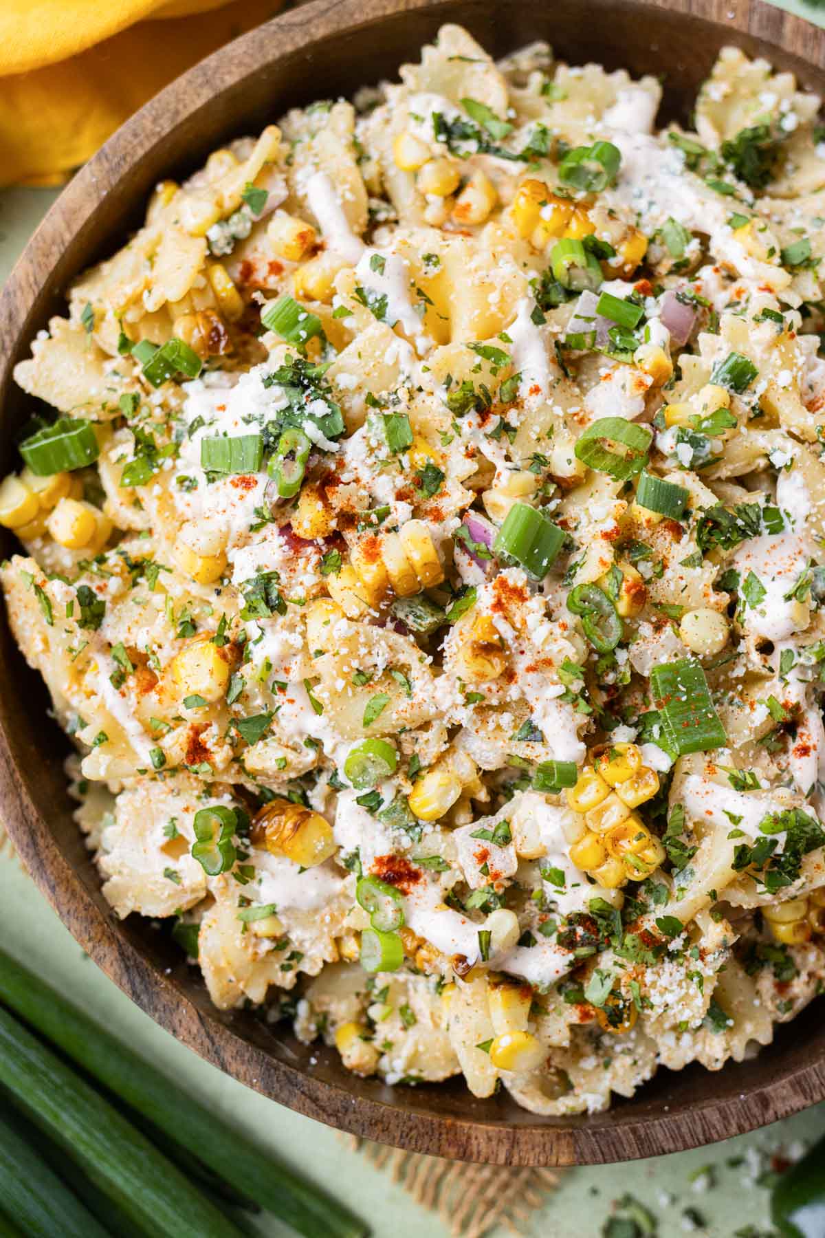 A Mexican Street Corn Salad is being served in a wooden bowl with a spoon.