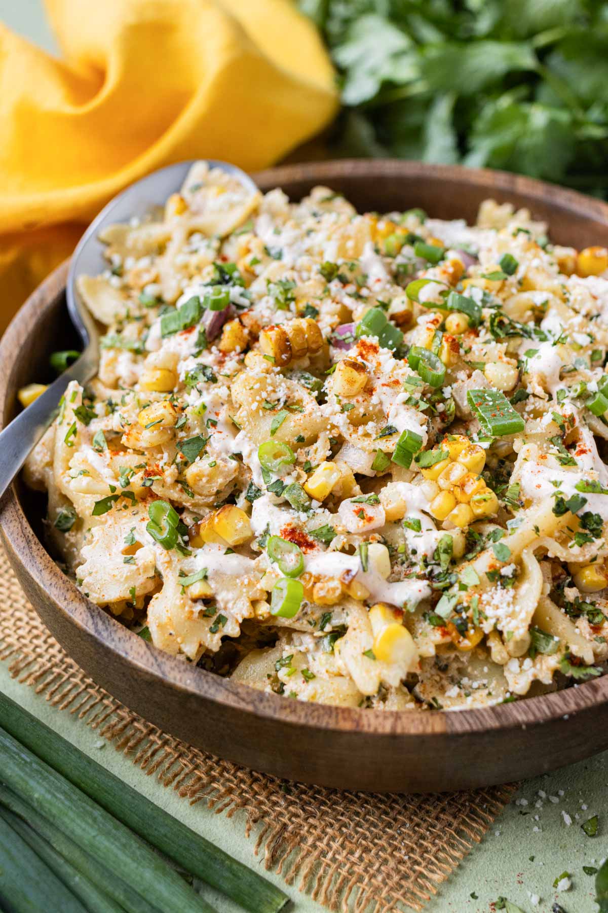 A wooden bowl is serving a Mexican Street Corn Pasta Salad with cilantro and green onions on top.