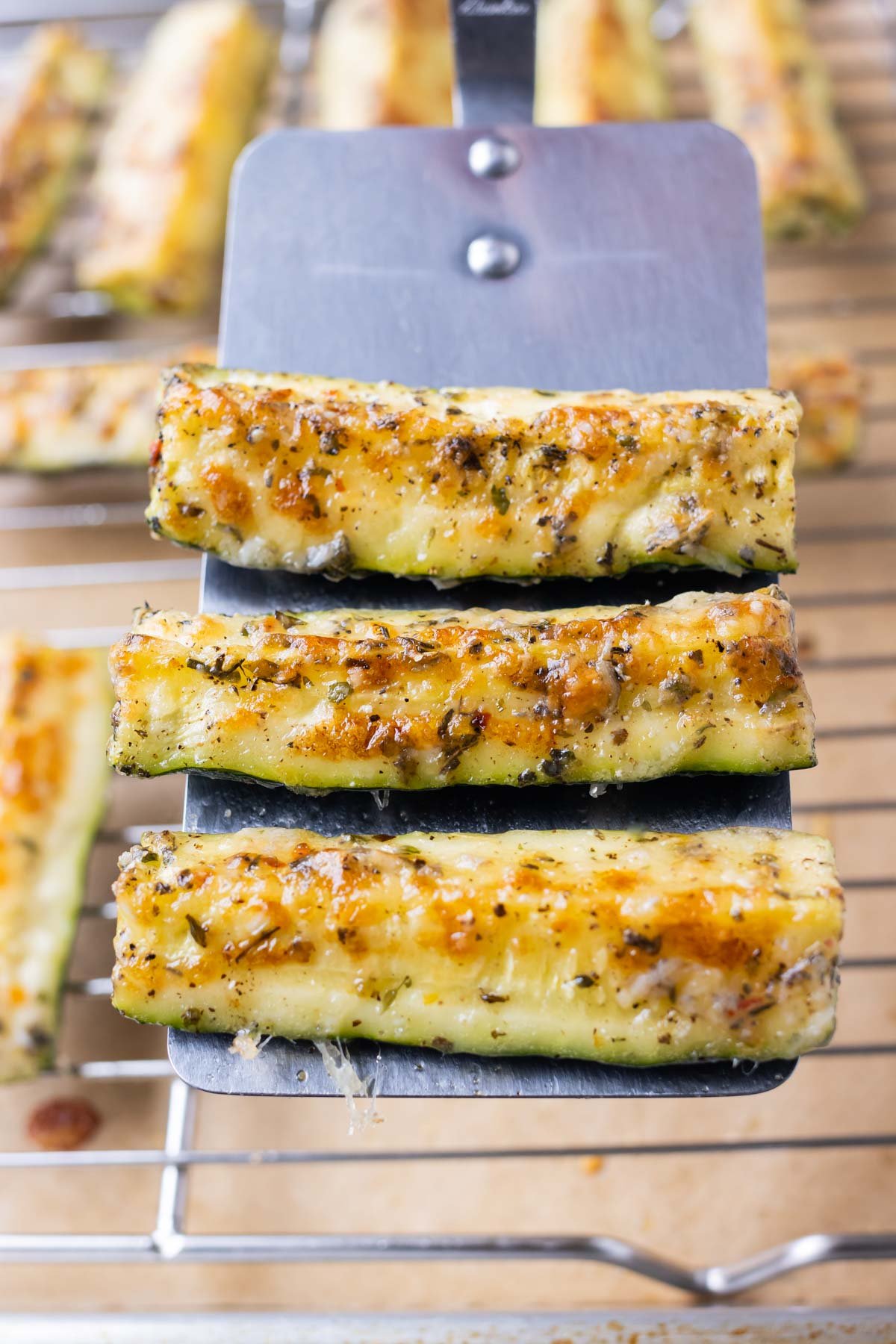 A spatula picks up 3 pieces of Parmesan crusted zucchini.