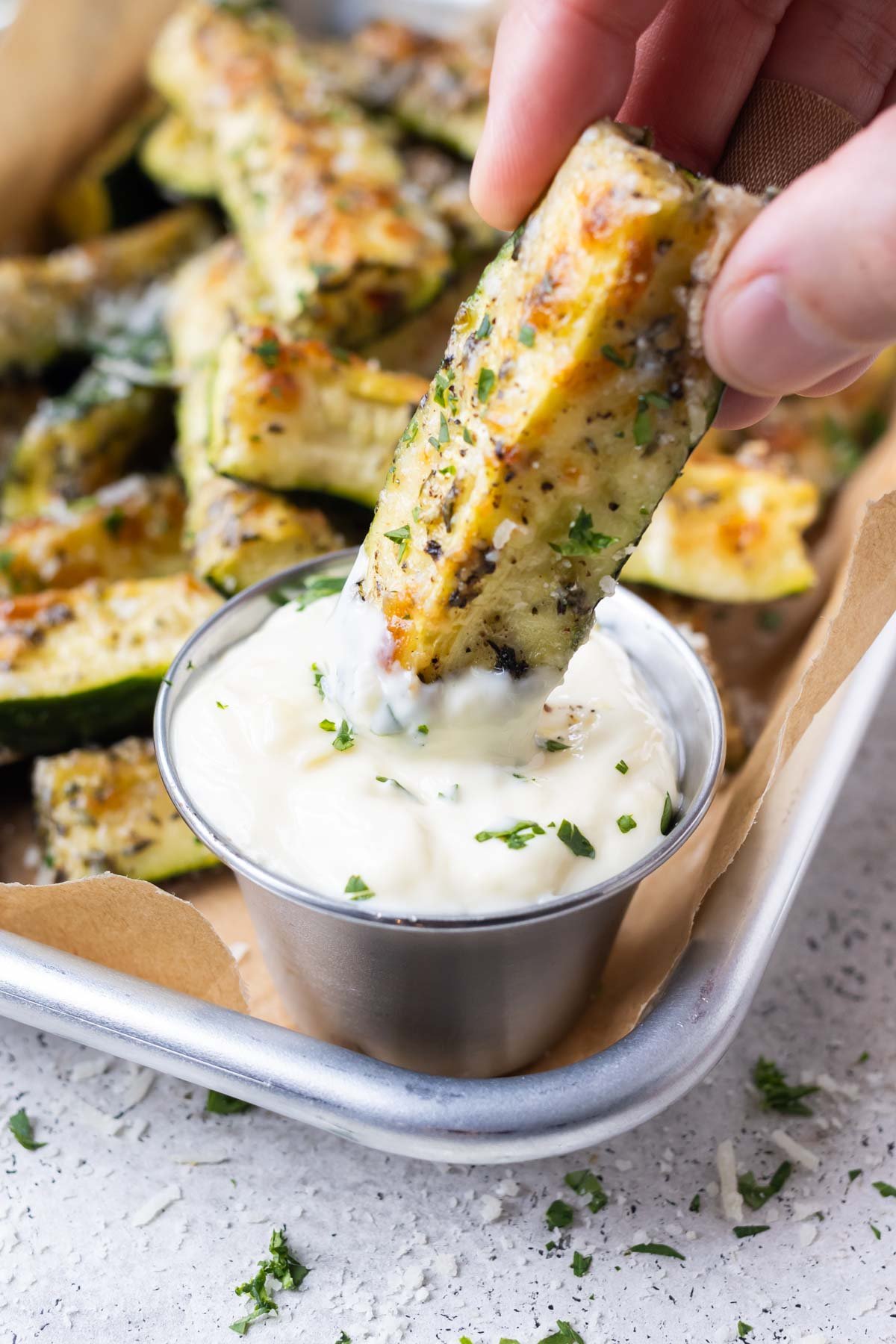 A hand dips a piece of zucchini into a dipping sauce.