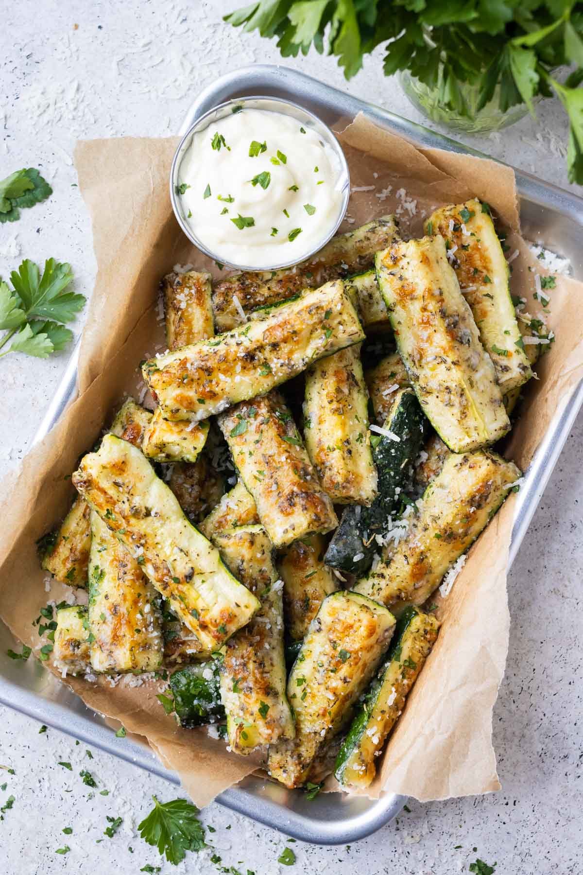 Parmesan crusted zucchini fries are served on a tray with a garlic aioli on the side.