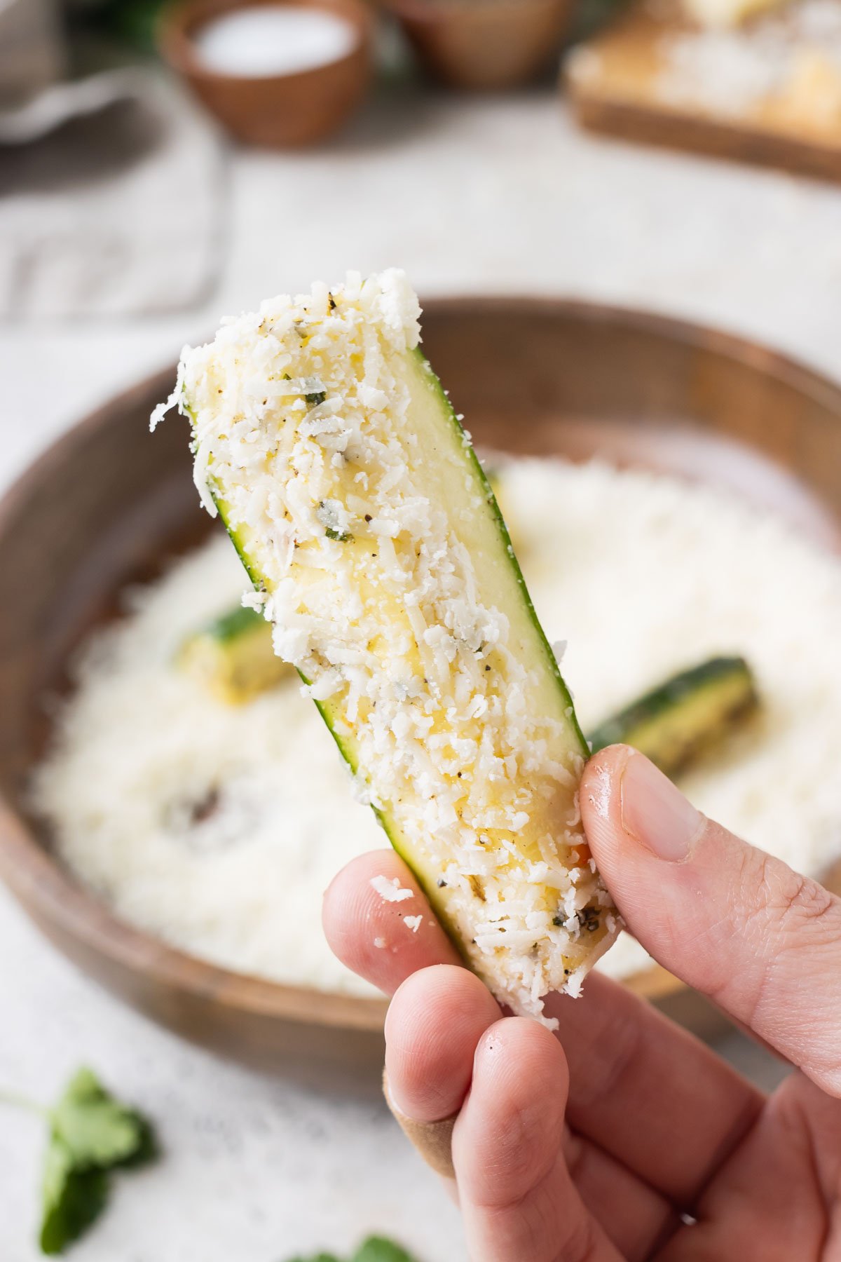 A hand picks up a slices of zucchini coated in Parmesan.