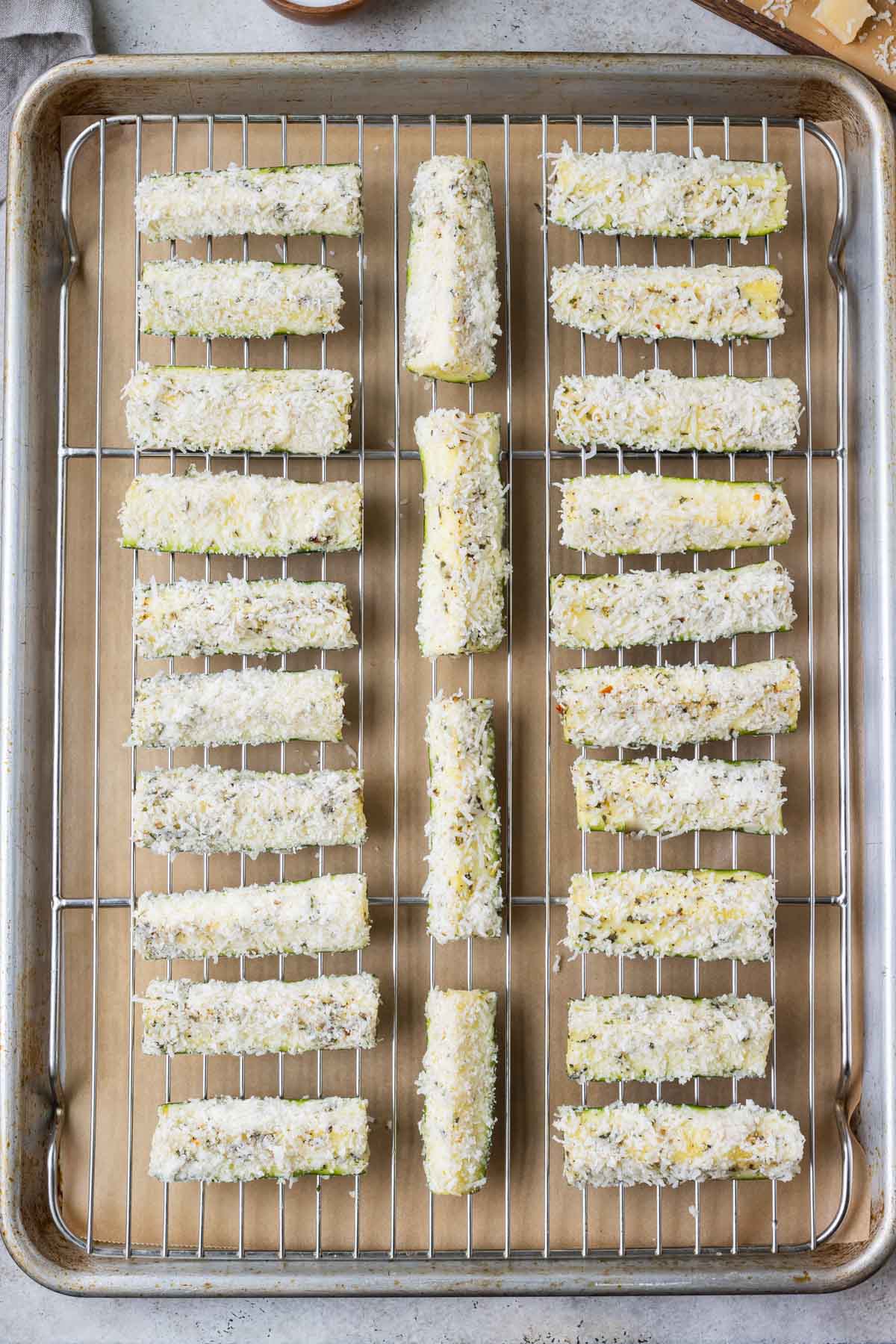 Parmesan crusted zucchini is spread on a baking dish before cooking in the oven.