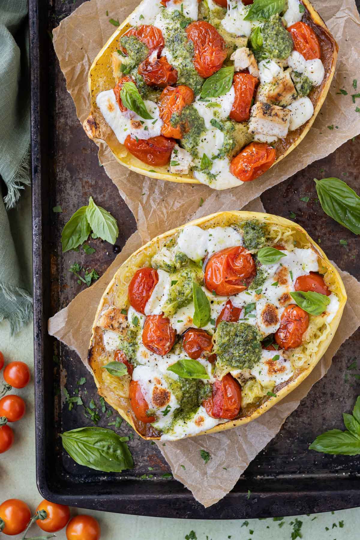Pesto chicken stuffed spaghetti squash halves are served with tomatoes and mozzarella cheese for dinner.
