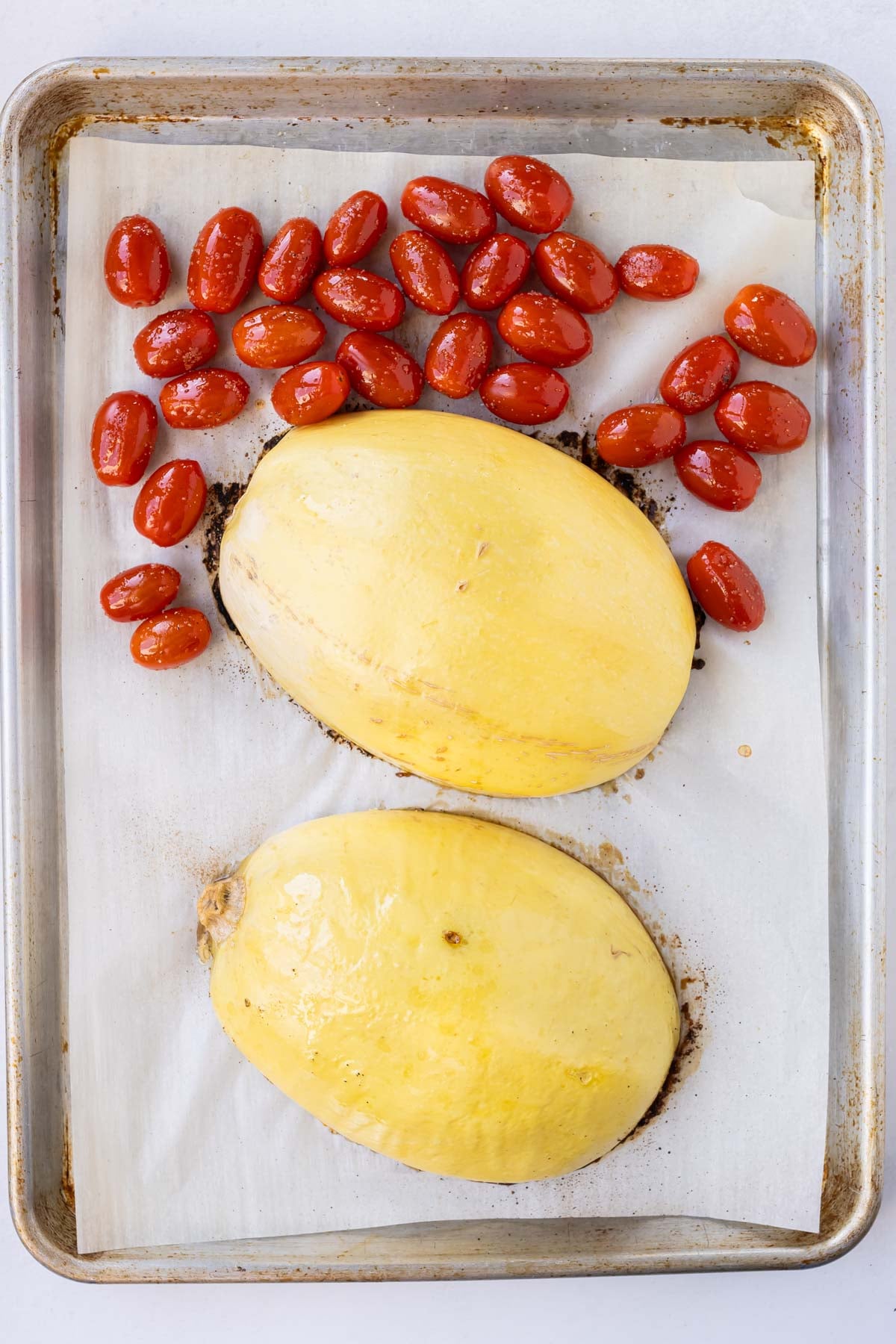 Tomatoes are added to a baking sheet with spaghetti squash.
