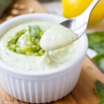 A spoon scoops up a bit of pesto mayo from a serving bowl.