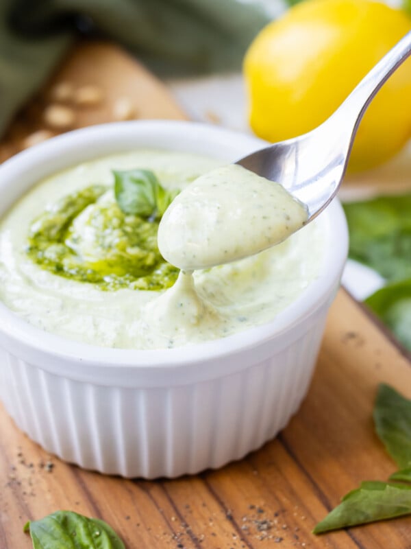 A spoon scoops up a bit of pesto mayo from a serving bowl.