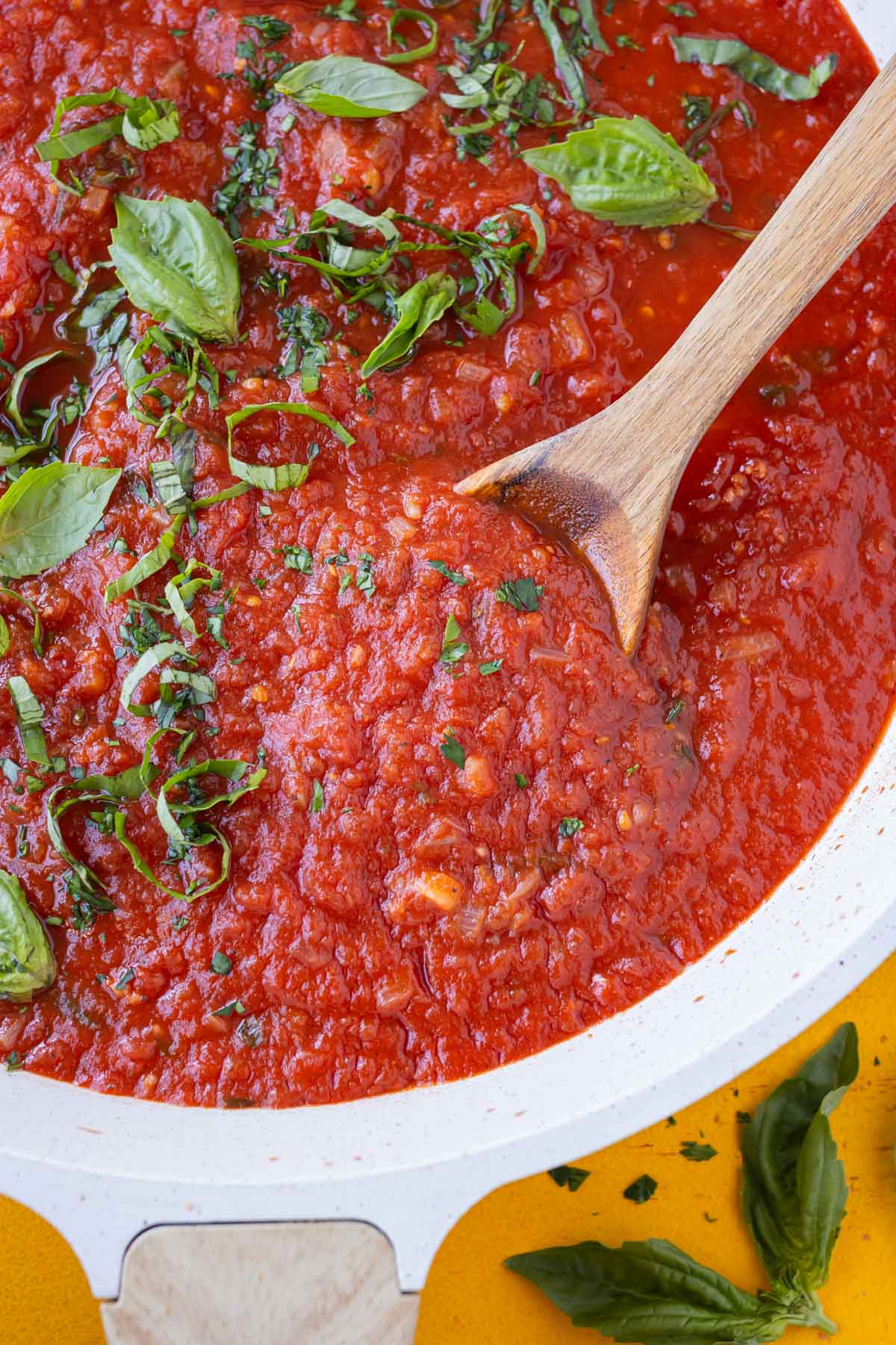 A wooden spoon is used to stir a skillet full of San Marzano tomato sauce with fresh basil.