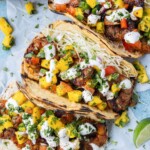 Shrimp tacos with mango salsa are served with lime wedges and cilantro.