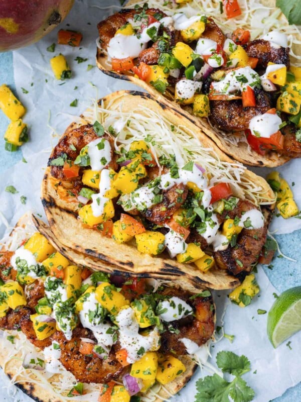 Shrimp tacos with mango salsa are served with lime wedges and cilantro.
