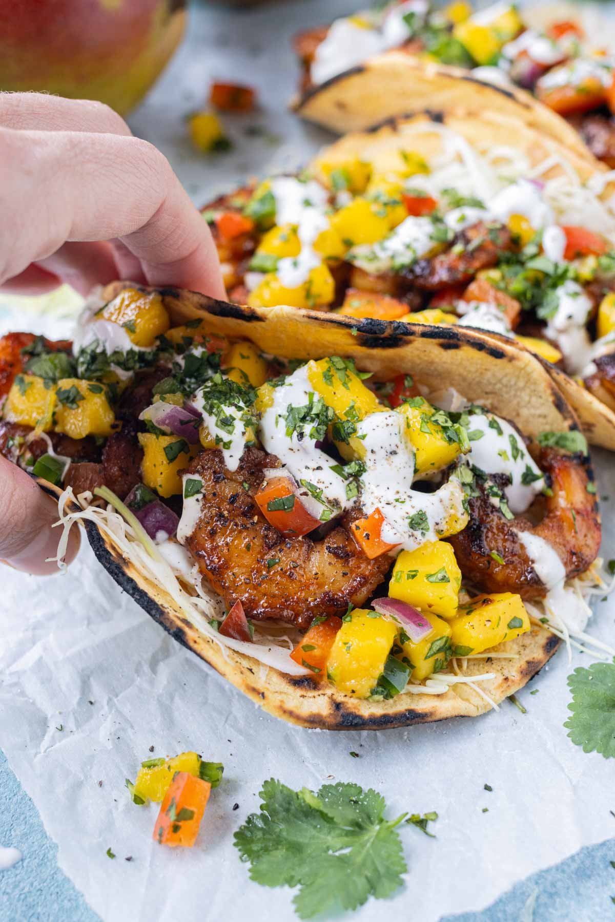 A hand is picking up a shrimp taco with mango salsa and cabbage slaw.