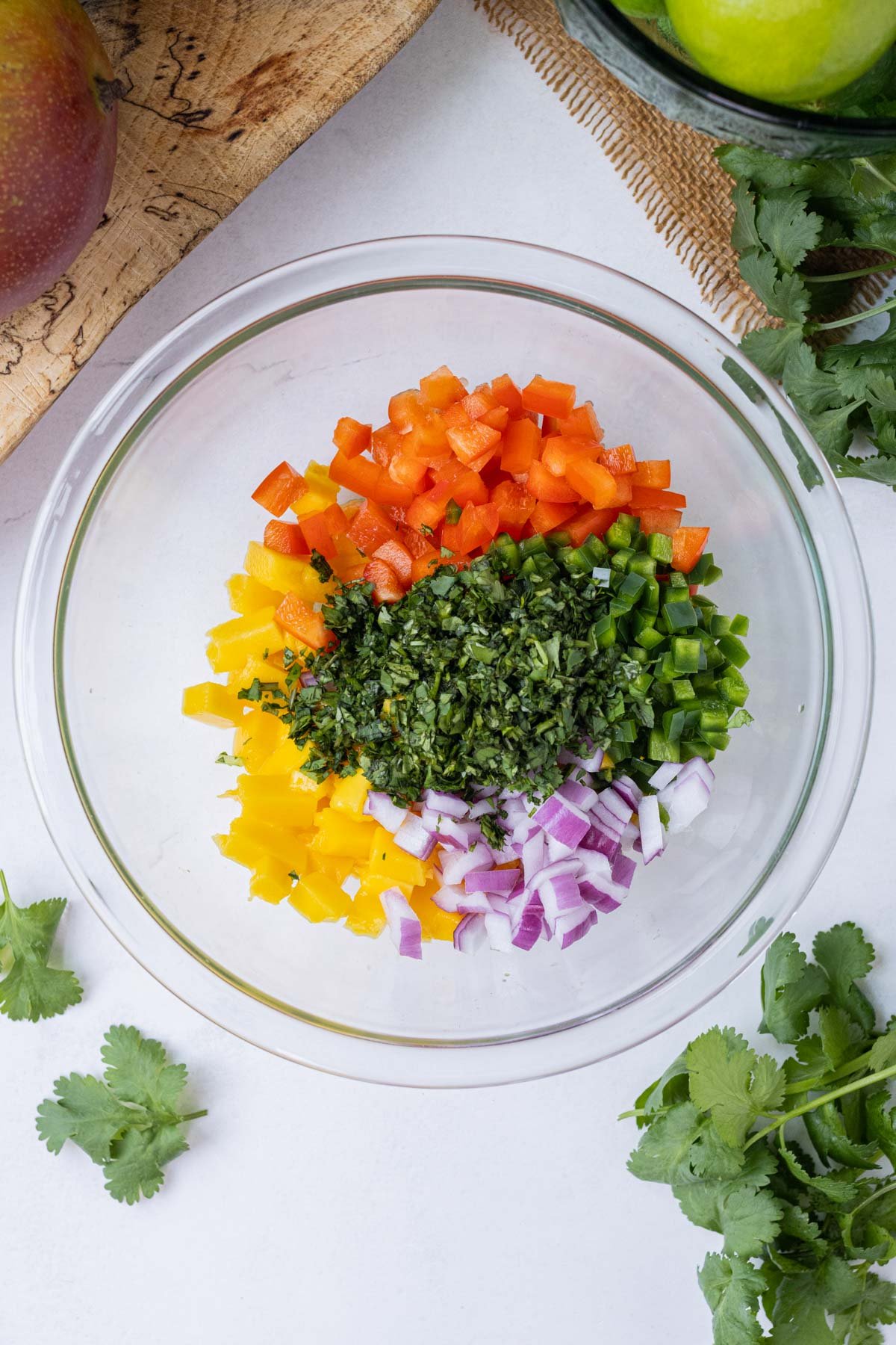 Mango salsa ingredients are added to a clear glass bowl.