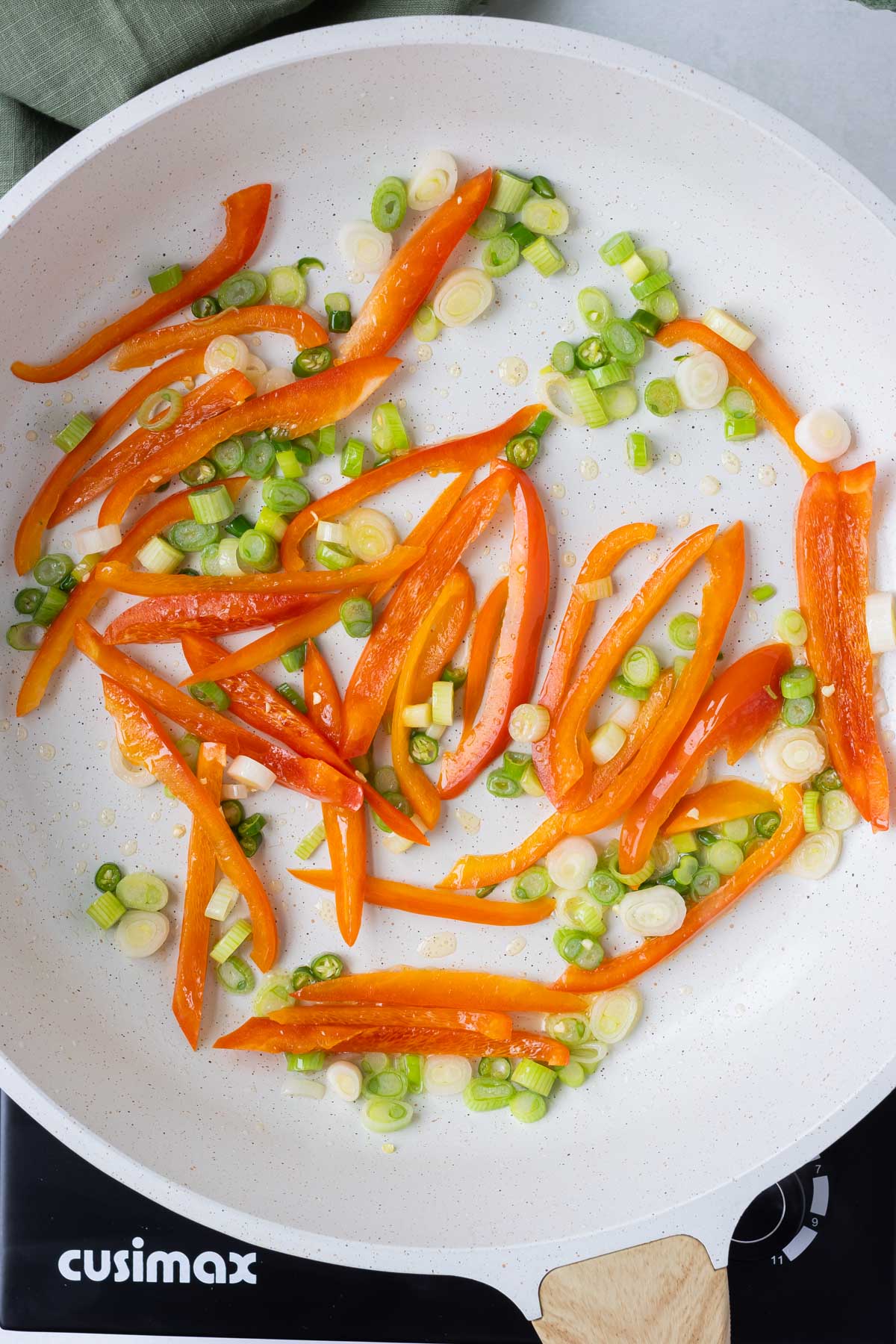 Green onions and peppers are cooked in a skillet.