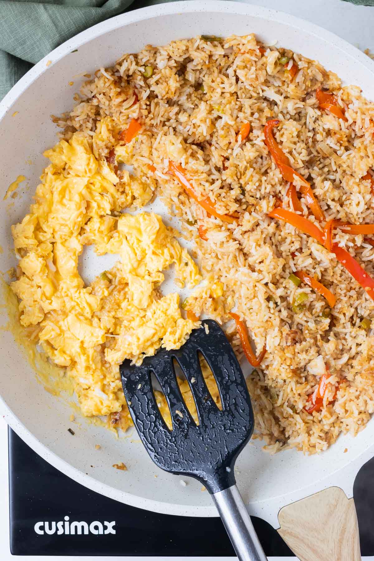 Scrambled eggs are added to the fried rice in the skillet.