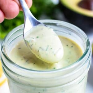 Avocado ranch dressing is picked up with a spoon from a mason jar.