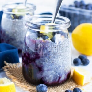 A glass jar full of a lemon blueberry chia seed pudding recipe is on a counter next to fresh blueberries.
