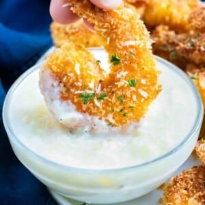 A fried coconut shrimp is being dipped into a piña colada sauce recipe like Red Lobster's.