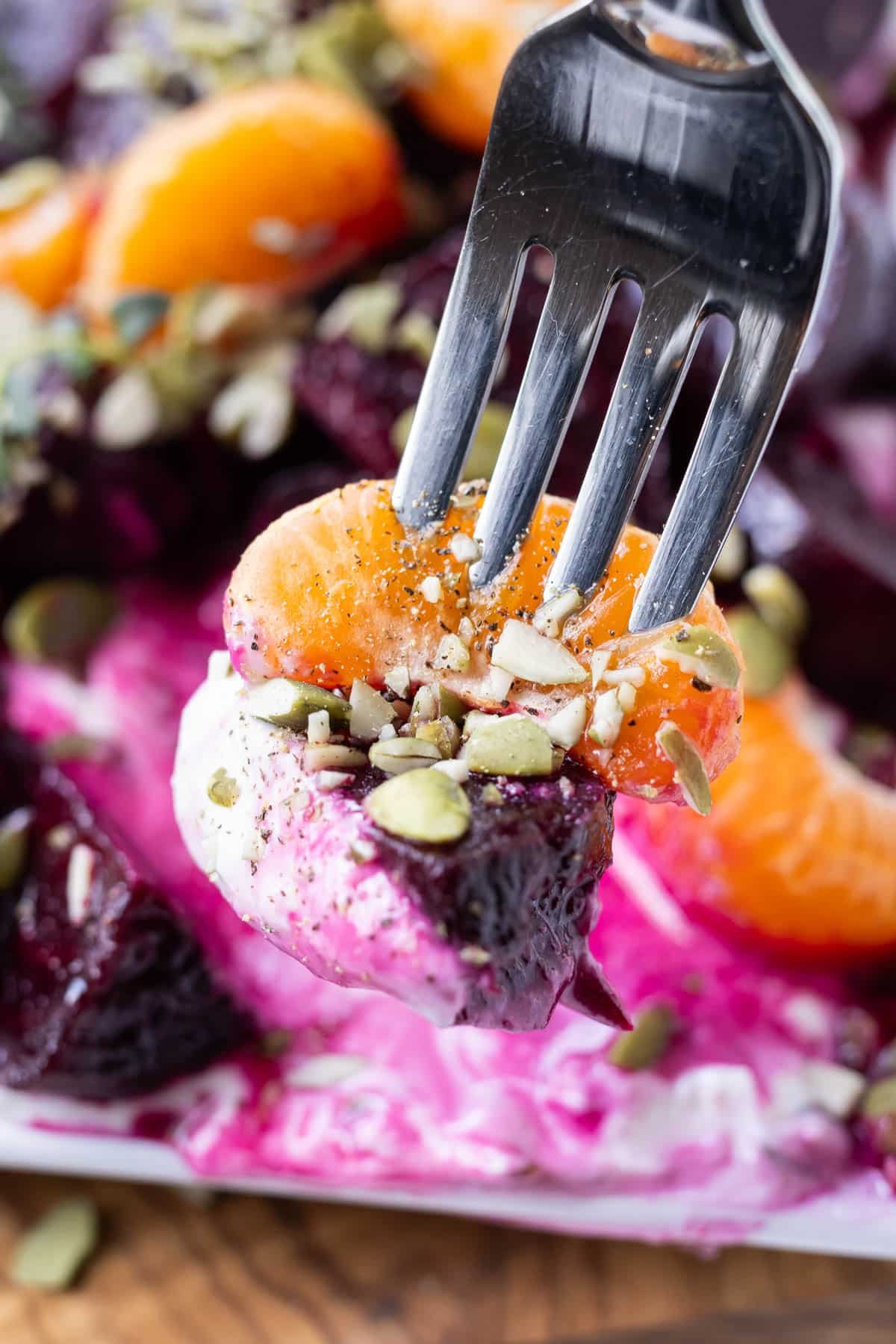 A fork holds a roasted beet and orange wedge to the camera.