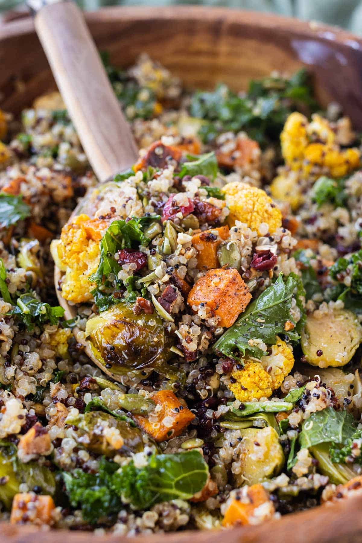 A wooden spoon is used to serve this warm fall quinoa salad.
