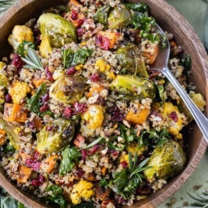 A wooden bowl is full of a Warm Fall Quinoa Salad with kale, roasted cauliflower and sweet potatoes and an apple cider vinaigrette.