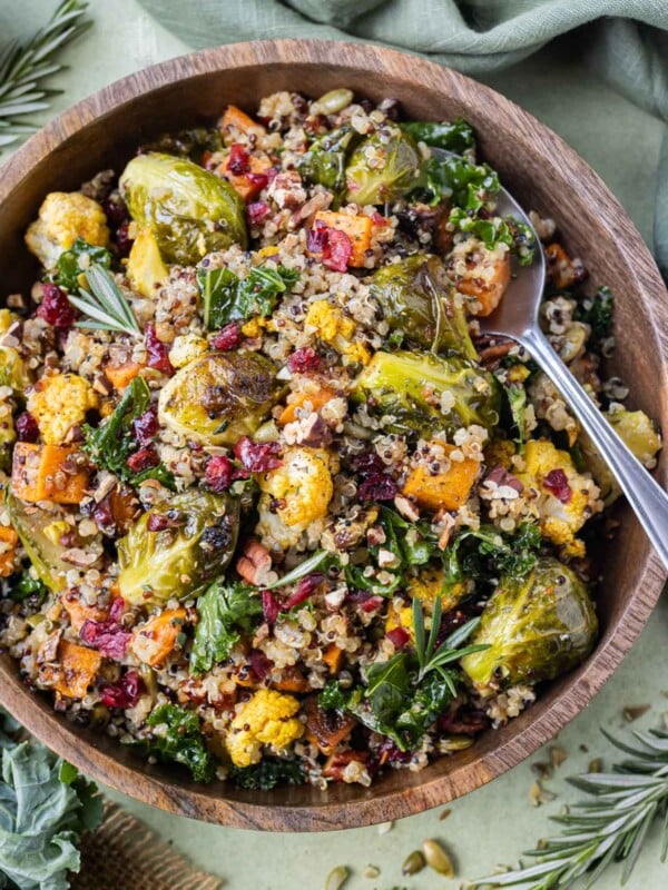 A wooden bowl is full of a Warm Fall Quinoa Salad with kale, roasted cauliflower and sweet potatoes and an apple cider vinaigrette.