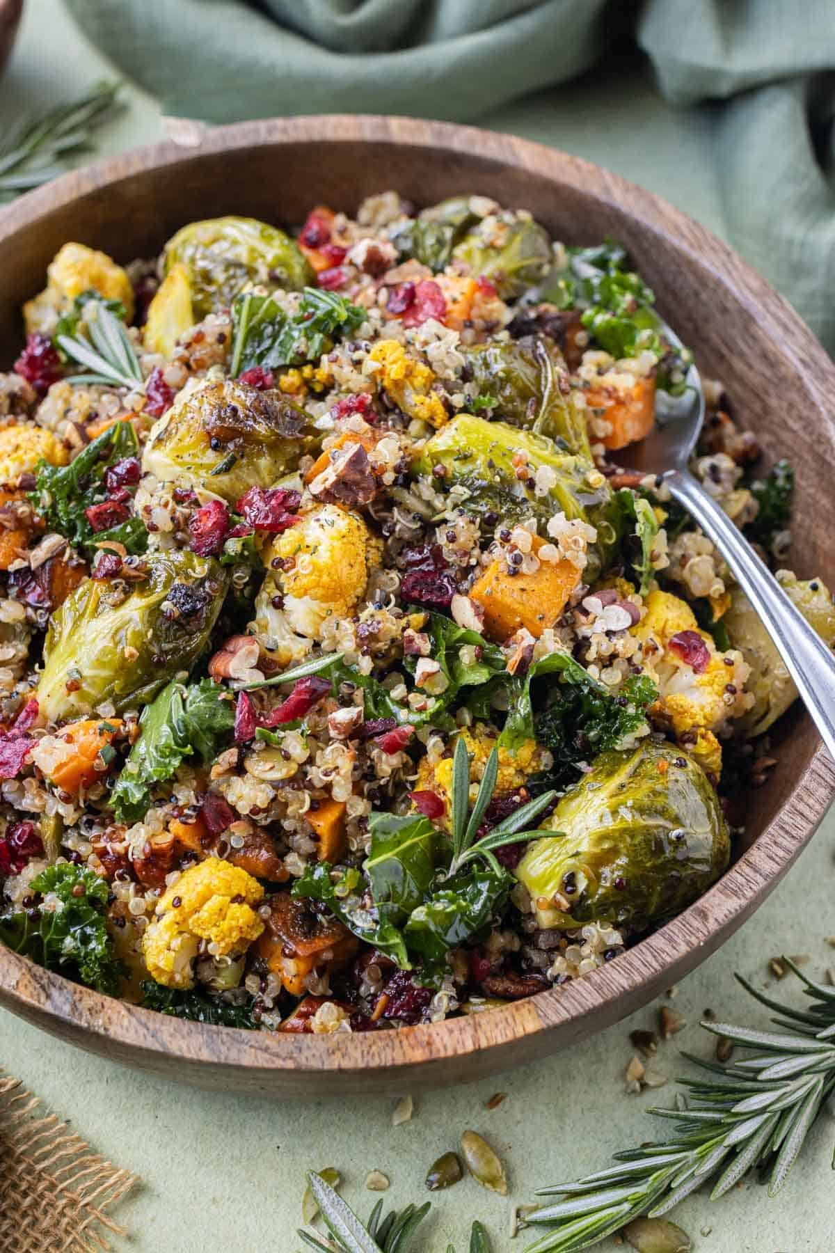 A wooden bowl is full of a warm Fall quinoa salad with kale, roasted cauliflower, Brussels sprouts, and sweet potatoes for a holiday recipe.
