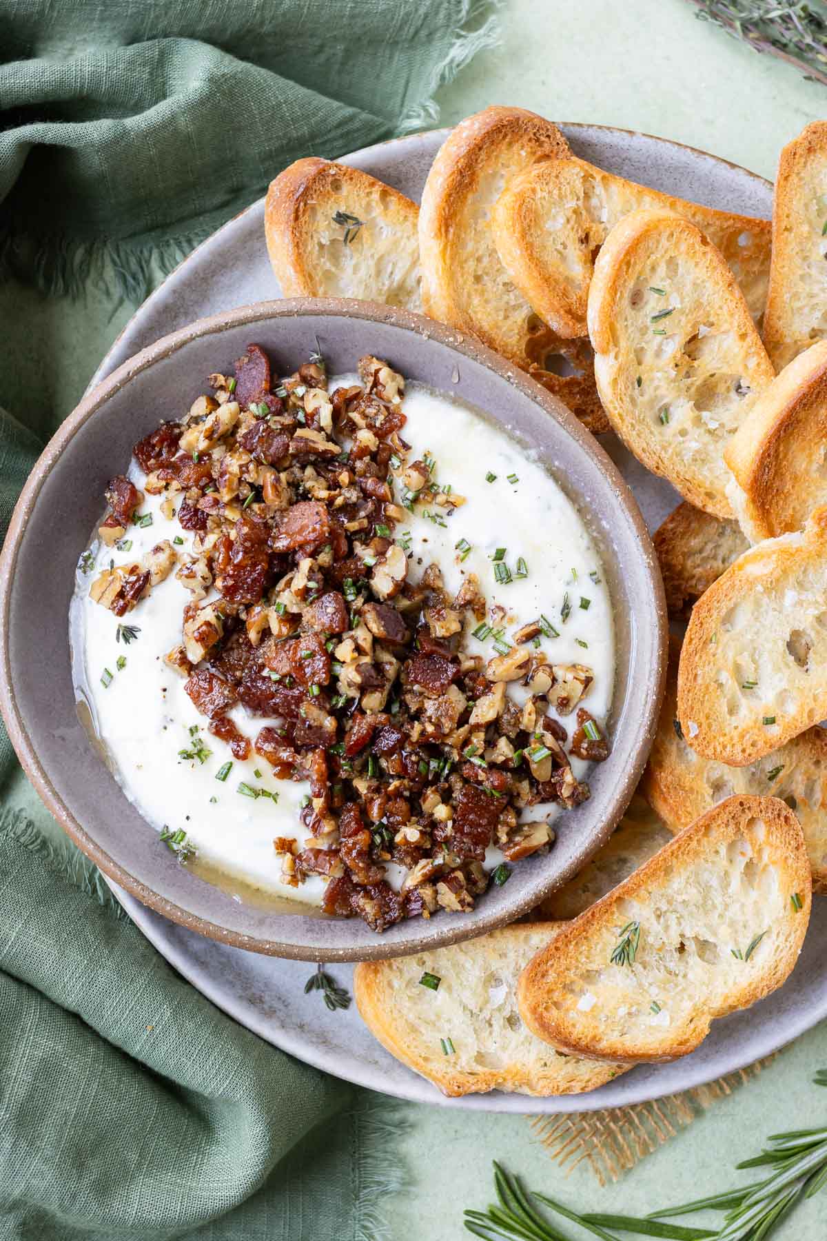 An appetizer bowl is being served full of whipped honey goat cheese with bacon and pecans next to crackers.