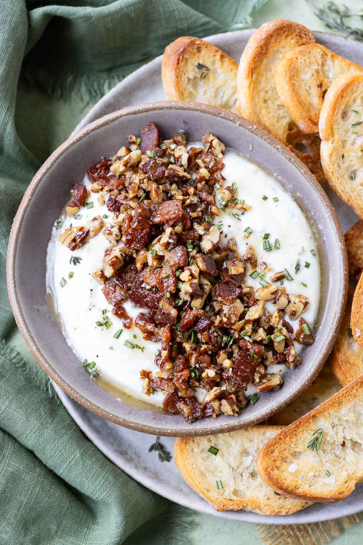 A bowl is full of whipped goat cheese, topped with candied bacon and pecans, and served with bread.