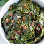 Southern collard greens with bacon are served in a white bowl with onions.