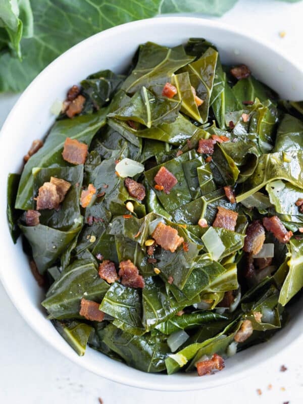 Southern collard greens with bacon are served in a white bowl with onions.